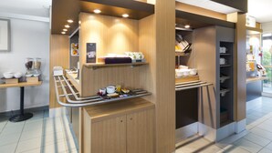 A modern breakfast area with wooden counters, a coffee machine, and a variety of breakfast items. - B&B HOTEL Rennes Nord Saint-Grégoire (Saint-Gregoire)