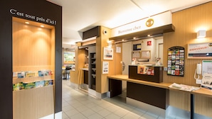 A reception area with a wooden reception desk, a glass partition, and a sign that reads "Bienvenue chez B&B." - B&B HOTEL Rennes Nord Saint-Grégoire (Saint-Gregoire)