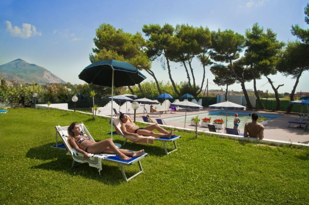 Un espace aménagé au bord de la piscine, avec des chaises longues et des parasols, une piscine et un paysage montagneux en arrière-plan.