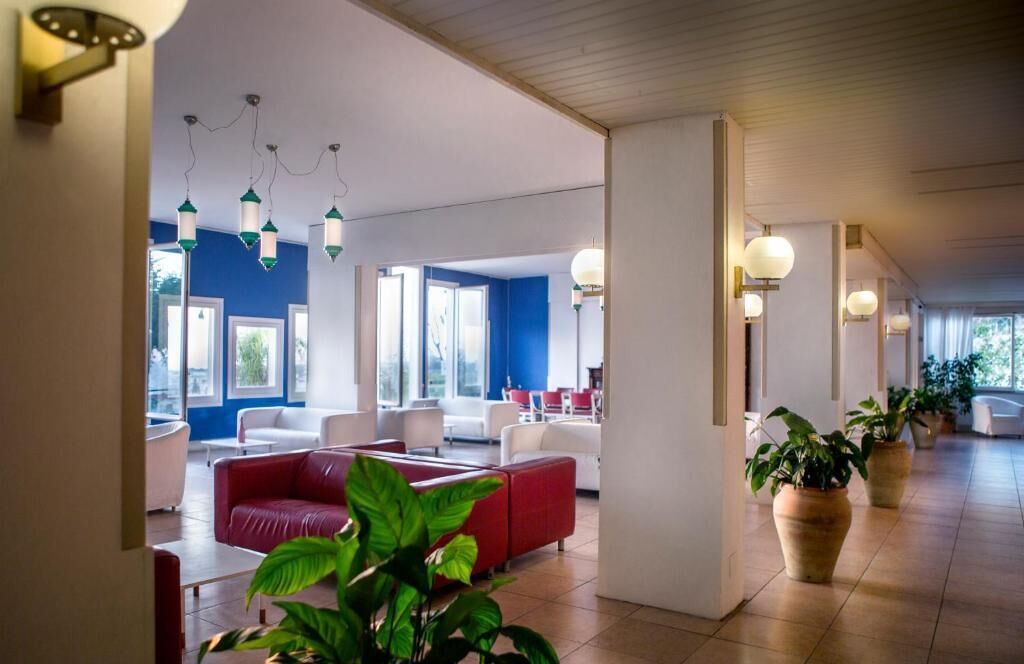 A modern hotel lobby with red and white seating, large windows, and potted plants.