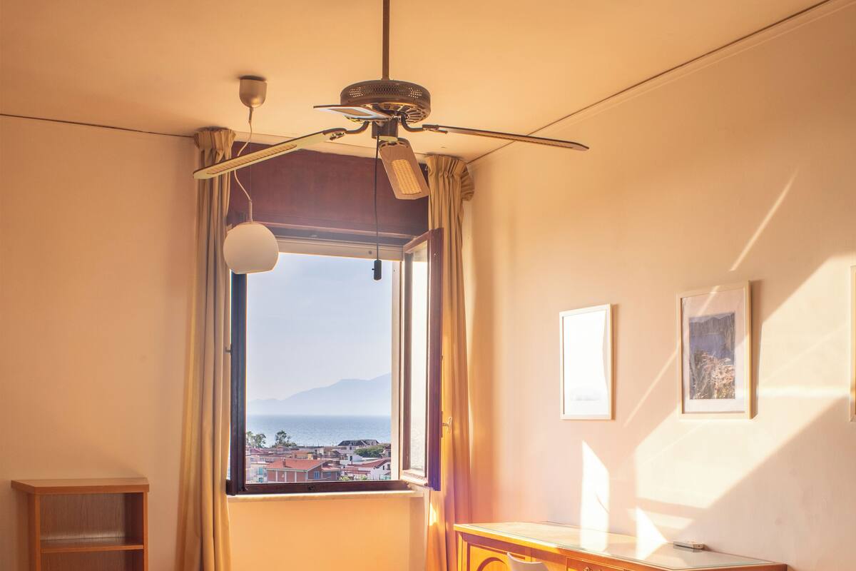 Habitación de hotel con dos camas, un escritorio, una silla, ventilador de techo y vista al mar.