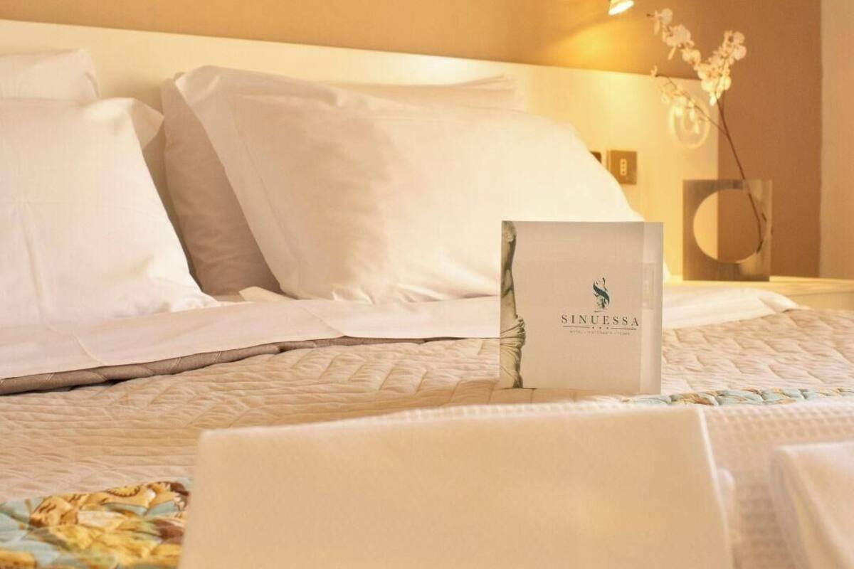 Una cama bien hecha con sábanas blancas, un cuadro floral encima y una fotografía enmarcada en la mesita de noche.