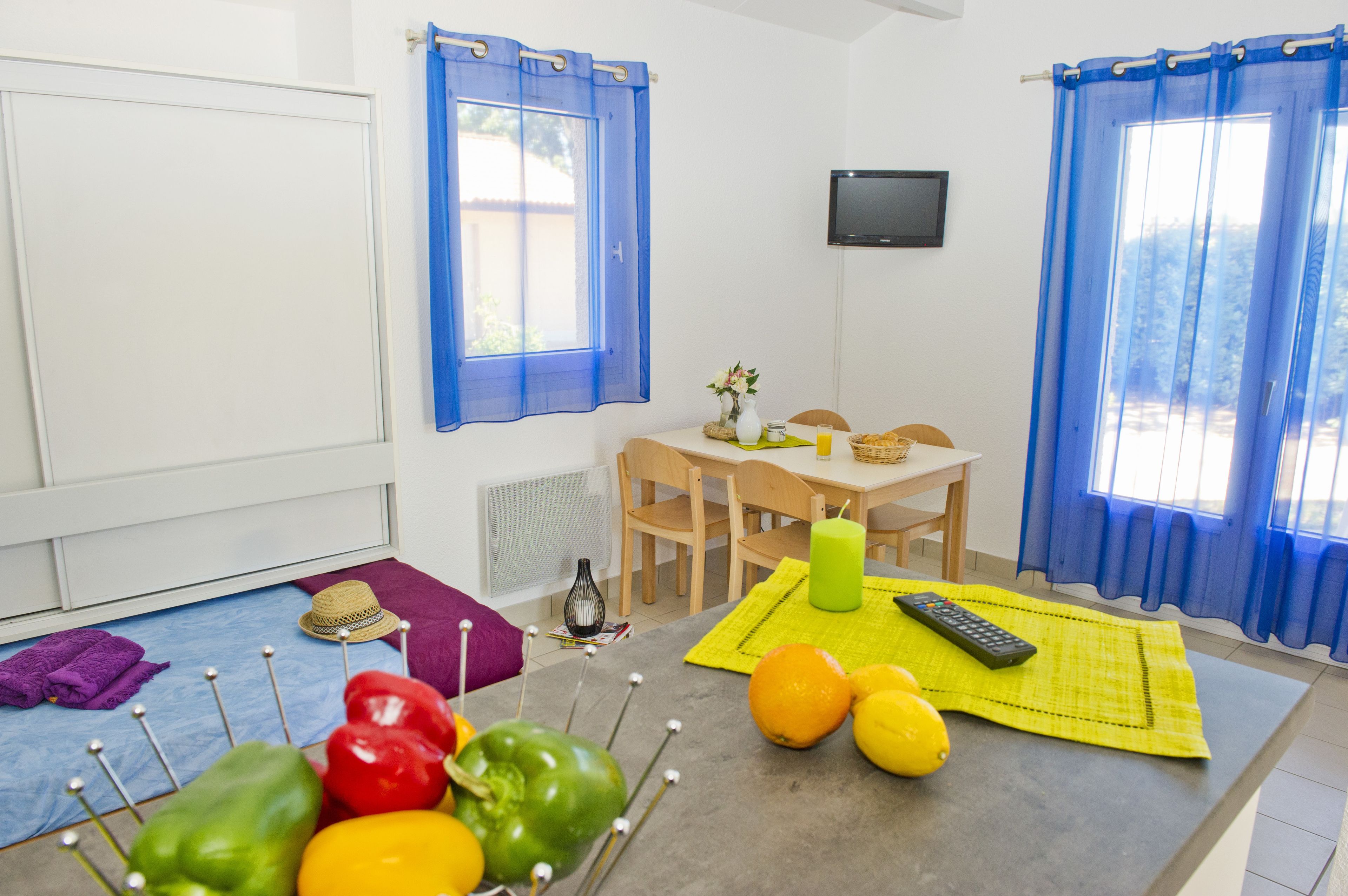 A room with a dining table, chairs, a TV on the wall, and a window with blue curtains.