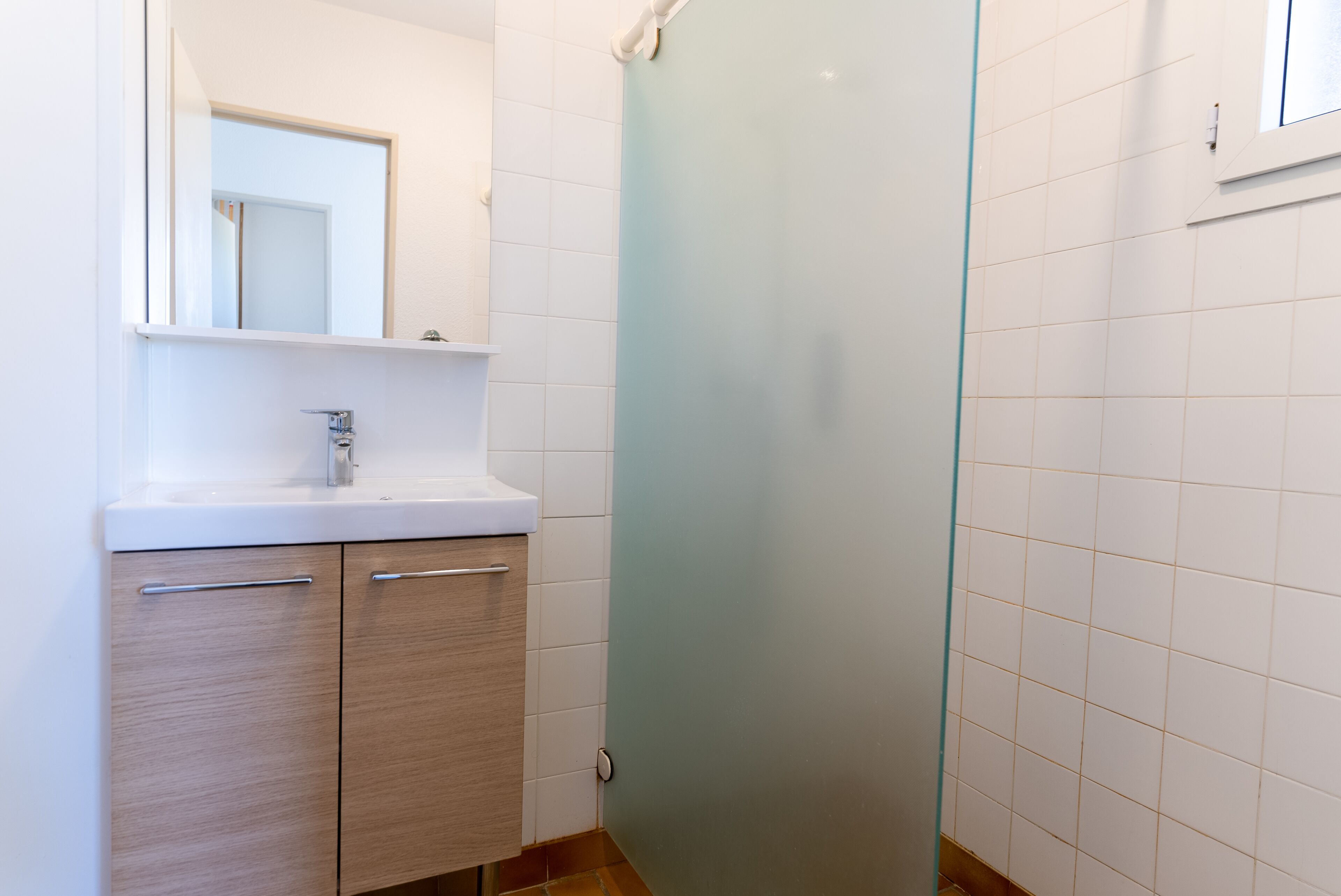 A bathroom with a white sink, wooden cabinets, and a frosted glass shower door.