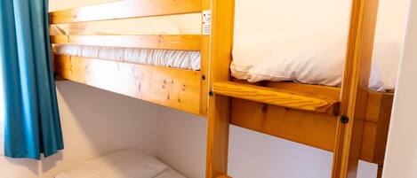 Una cama litera con escalera, ropa de cama blanca y cortina azul.