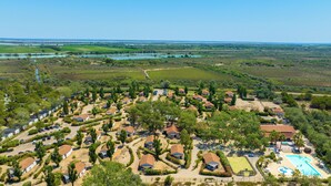 An aerial view of a residential area with houses arranged in rows, a swimming pool, and a river in the background. - Azureva Le Grau du Roi (Le Grau-Du-Roi)