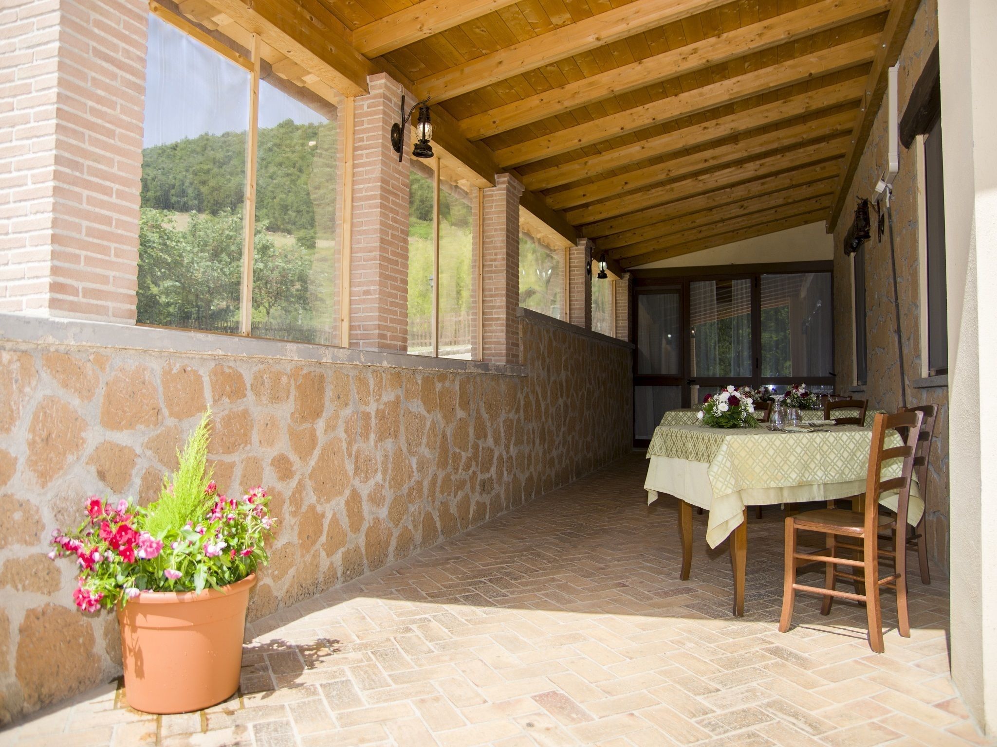 An outdoor patio with a table set for dining, stone walls, and a view of greenery.