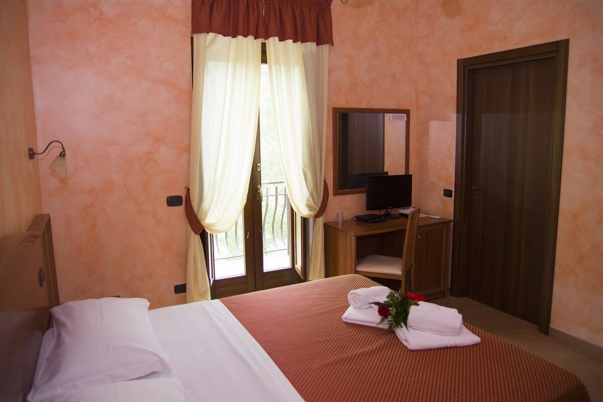 A hotel room with a bed, a desk with a computer, a mirror, and a wardrobe.