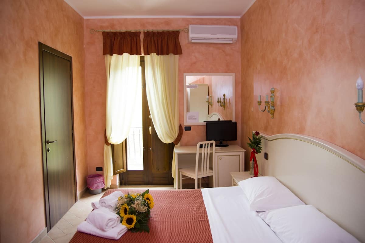 A hotel room with a bed, a desk with a chair, a television, and a mirror.