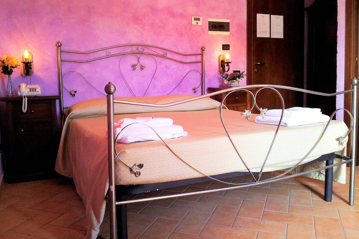 A bed with a metal frame, a bedside table with a lamp, and a wall clock.