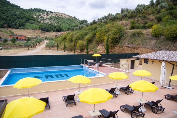 Zona de piscina con sombrillas amarillas, sillas de descanso y vistas del paisaje circundante.