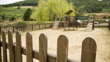 Explore the playground area with a climbing structure and slide, surrounded by a sandy surface and lush greenery.