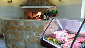 A stone counter with a glass display case containing various meats and a fire in the background. - Agriturismo La Rocca dei Briganti (Rocca Massima)