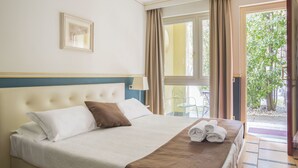 A neatly made bed with a brown throw blanket and rolled towels, a framed picture on the wall, and a view of the outdoors through a door. - Hotel Ponte di Rialto (Crema)