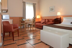 A hotel room with a bed, a sofa, a dining table with chairs, a TV, and lamps.