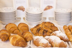 A variety of pastries displayed on trays, with stacks of plates in the background.