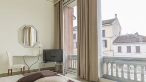 A hotel room with a bed, a television on a stand, a chair, a desk, and a large window with a view of buildings. - Hotel Ponte di Rialto (Crema)