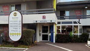 A hotel entrance with a sign indicating room types and prices, a welcome sign, and a small garden area. - B&B Hôtel La Queue En Brie (La Queue-en-Brie)