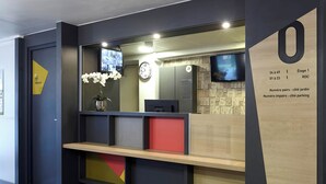 A reception desk with a clock, a TV, and a sign with room numbers and directions. - B&B Hôtel La Queue En Brie (La Queue-en-Brie)