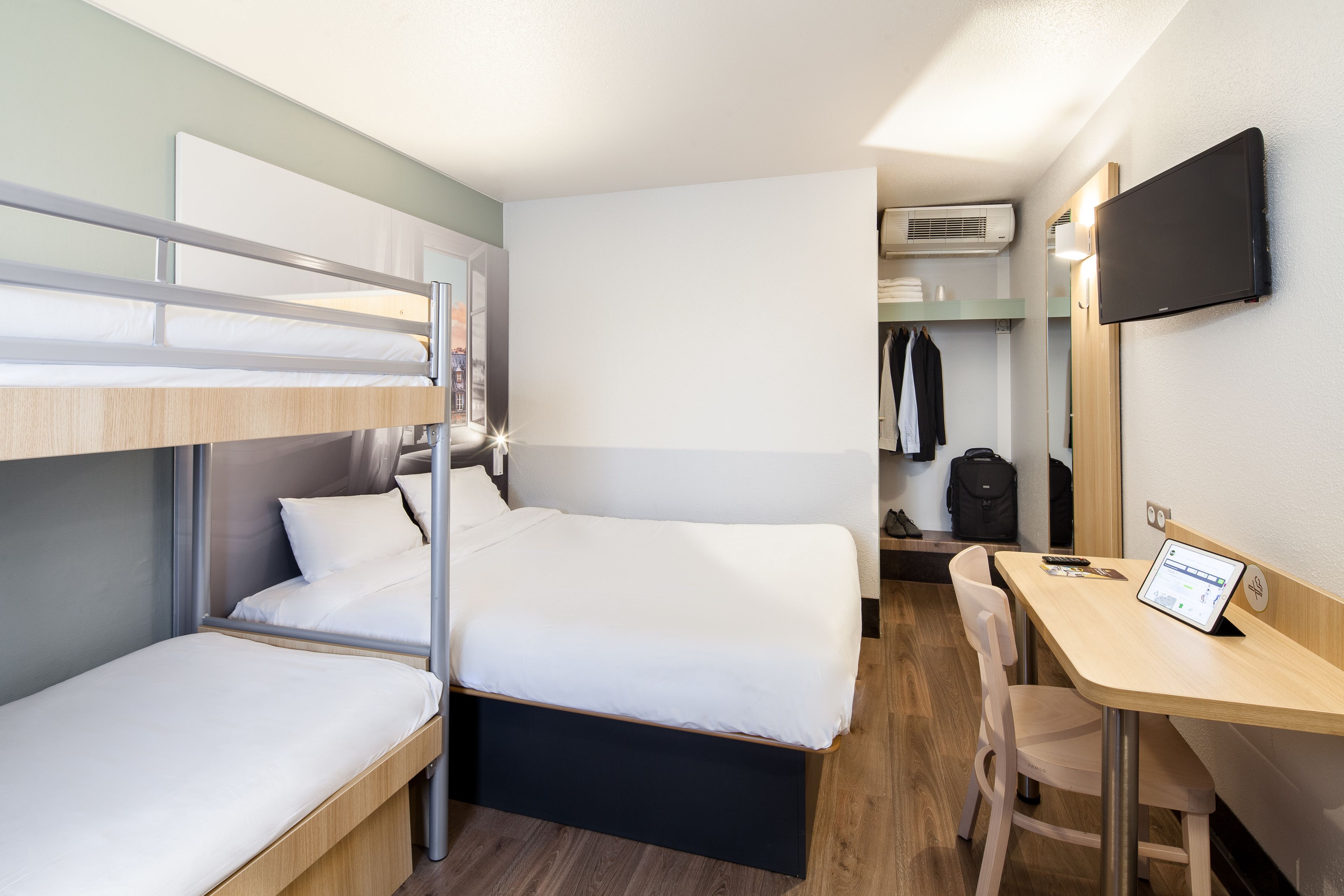 Une chambre d’hôtel compacte équipée de lits superposés, d’un bureau, d’une chaise, d’une télévision et d’une armoire.