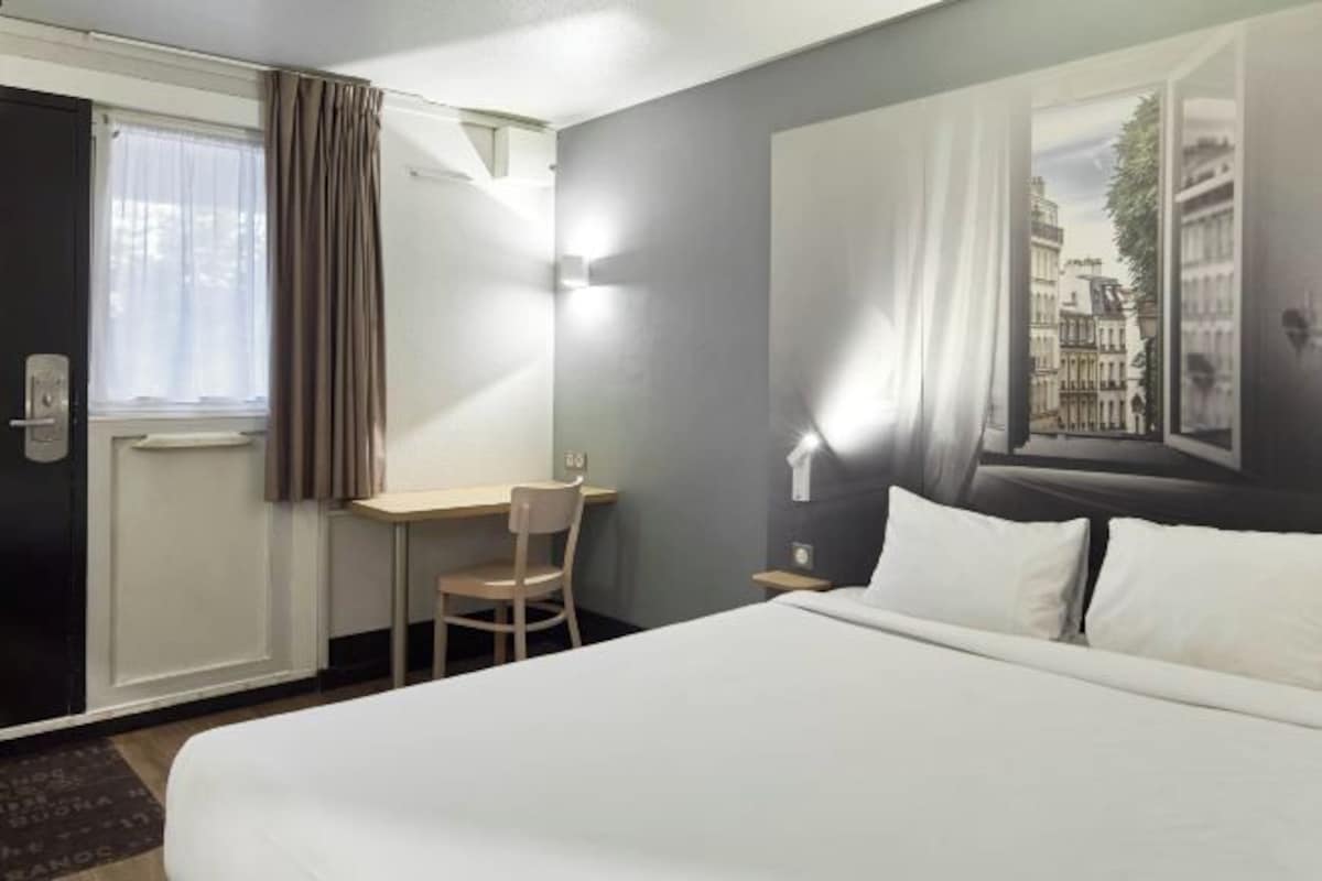 Een hotelkamer met een bed, een bureau, een stoel en een raam met gordijnen.