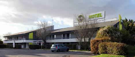 Un hôtel avec une enseigne, un parking et un espace vert.