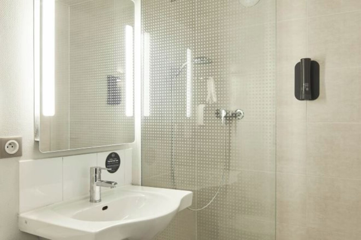 A modern bathroom with a white sink, a large mirror, and a glass shower enclosure.