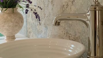 A white ceramic sink with a modern faucet, a vase with purple flowers, and a textured wall in the background.