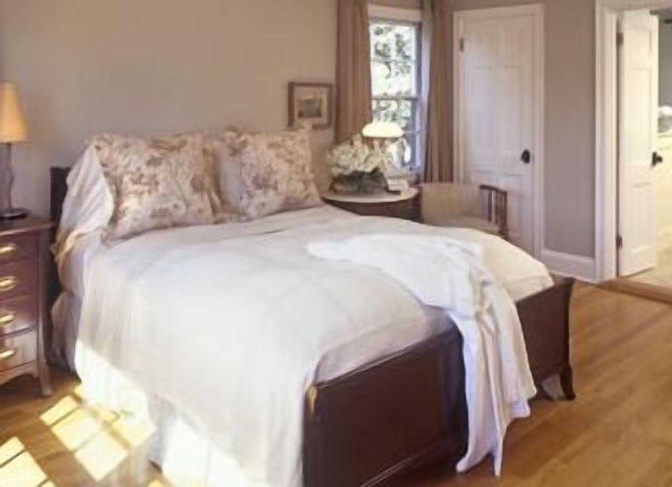 Un dormitorio con cama, mesita de noche, lámpara y ventana con cortinas.