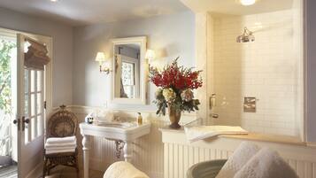 A bathroom with a sink, mirror, and shower. There are towels and toiletries on the counter.