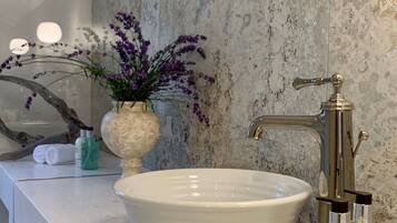 Une salle de bain avec un lavabo blanc, un mur en marbre et un miroir.