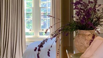 Un dormitorio con cama, cortinas, una ventana y un jarrón con flores.