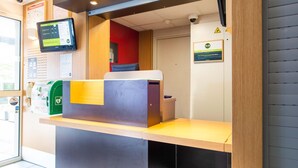 A reception desk with a digital screen, a telephone, and a sign indicating a 24-hour service. - B&B HOTEL Nantes Parc Expos La Chapelle (La Chapelle-sur-Erdre)