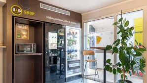 A B&B shop with a refrigerator stocked with beverages, a microwave, and a chair. - B&B HOTEL Nantes Parc Expos La Chapelle (La Chapelle-sur-Erdre)