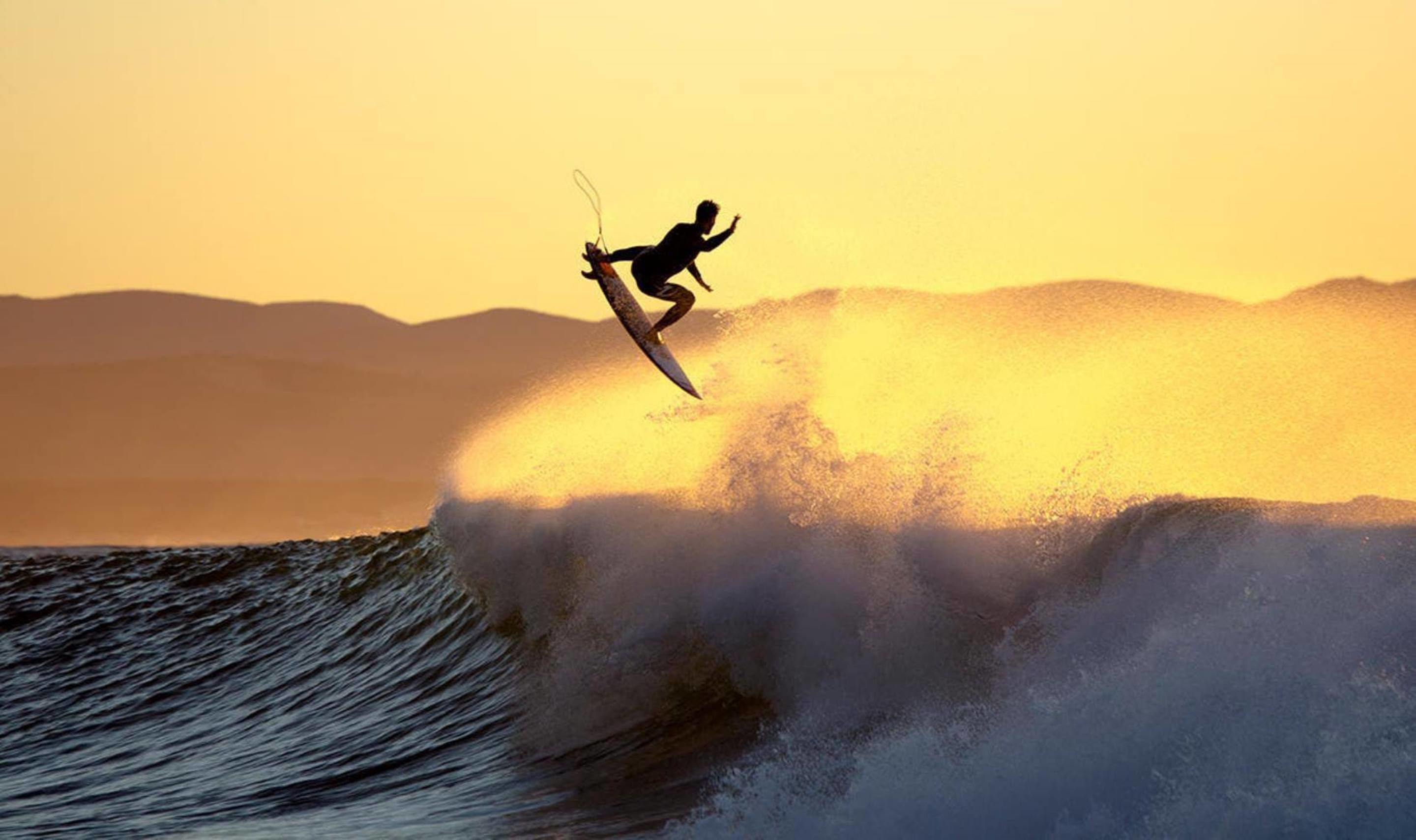 A surfer riding a large wave with mountains in the background.