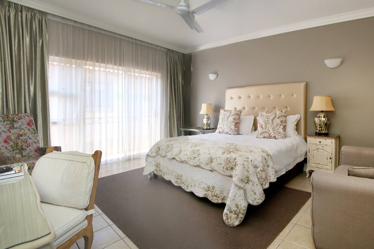 A hotel room with a large bed, two bedside tables with lamps, a chair, and a desk with a lamp.