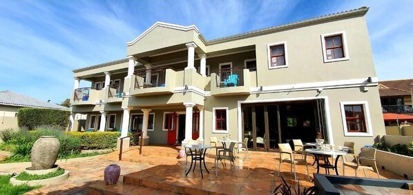 Edificio de dos pisos con un patio que cuenta con mobiliario exterior y una fuente de piedra.