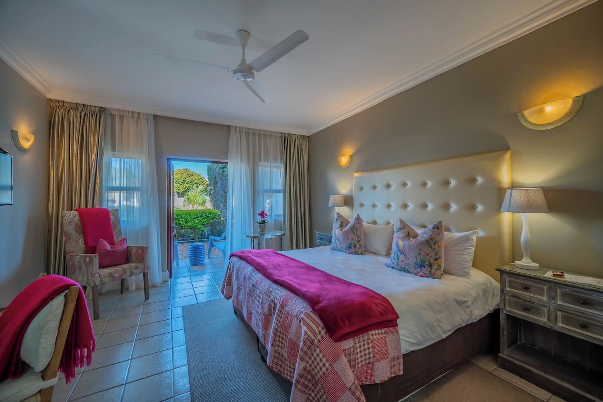 A bedroom with a large bed, a ceiling fan, a nightstand, a chair, and a view of the outdoors.