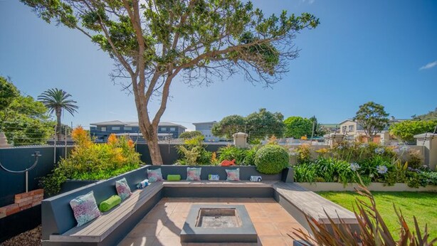 A modern outdoor patio with a built-in seating area, a fire pit, and lush landscaping. - The Mandyville (Jeffreys Bay)