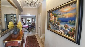 A hallway with a large mirror, a painting of a coastal scene, and a red rug leading to a dining area. - The Mandyville (Jeffreys Bay)