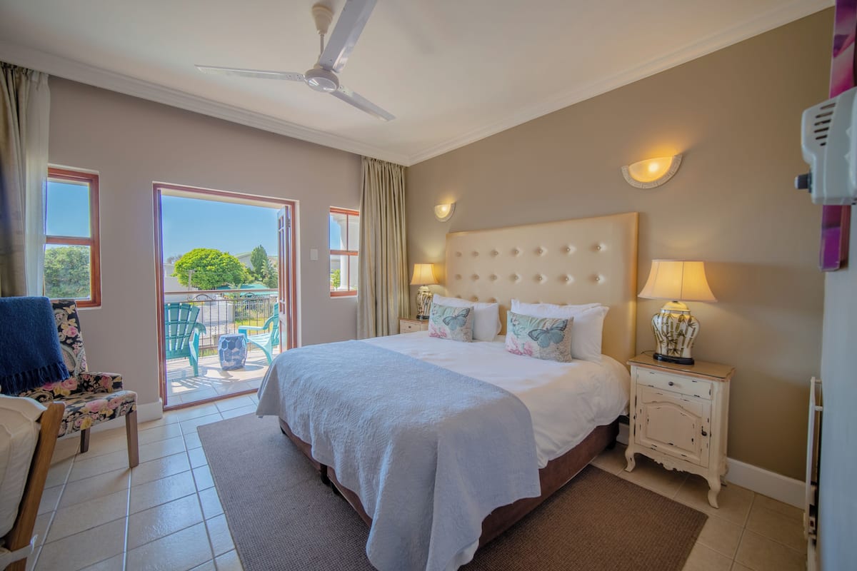 A bedroom with a large bed, a ceiling fan, a nightstand with a lamp, and a view of the outdoors through a sliding door.