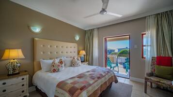 A hotel room with a large bed, two bedside lamps, a ceiling fan, a view to the outside, and a chair by the window.