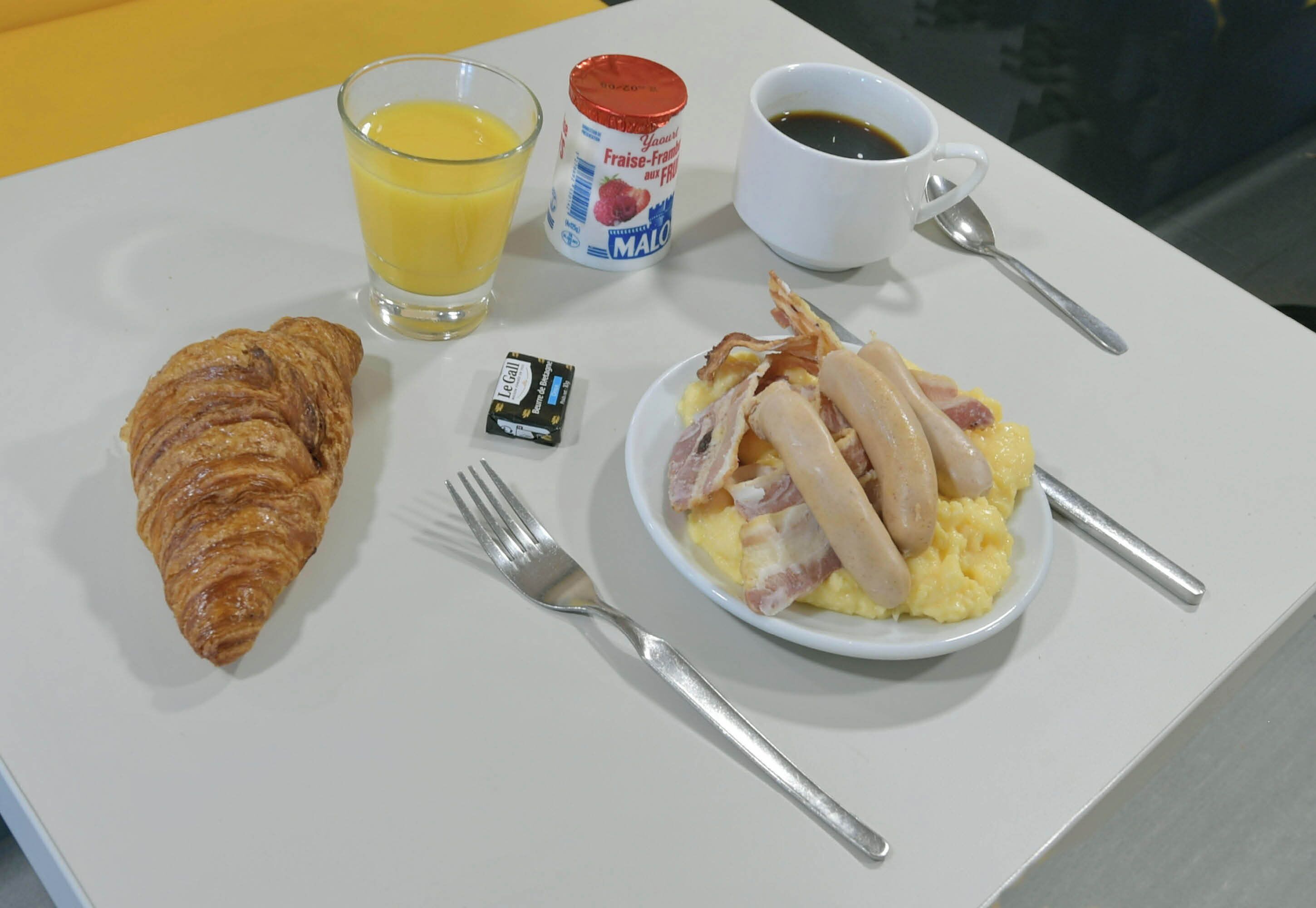A breakfast plate with croissant, scrambled eggs, bacon, and a glass of orange juice.