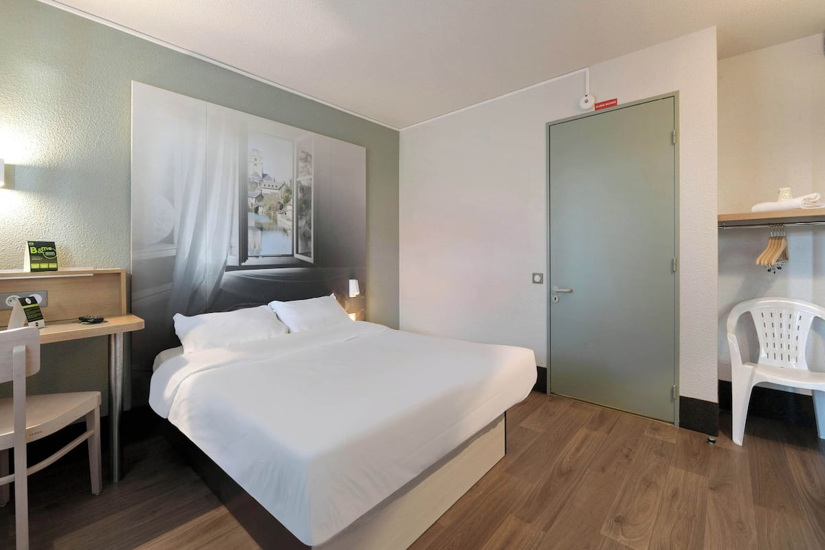 A hotel room with a bed, a desk, a chair, a wardrobe, and a door.