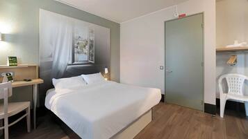 Een hotelkamer met een bed, een bureau, een stoel, een kledingkast en een deur.