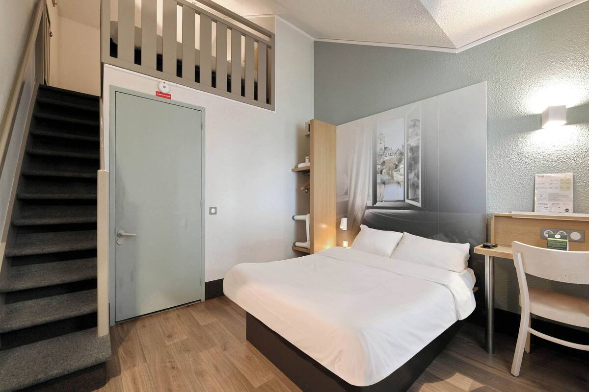 A bedroom with a bed, a desk, a chair, a staircase, and a door.