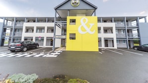 Un hotel con un letrero amarillo y blanco llamativo, varios pisos y un área de estacionamiento.
