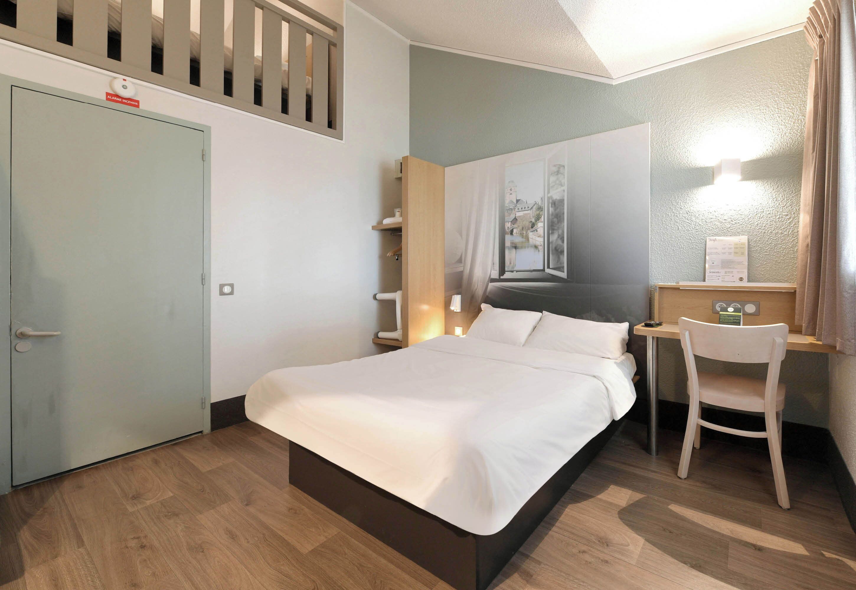 A hotel room with a bed, a desk, a chair, a wardrobe, and a window with a view.