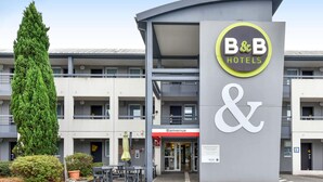 A B&B hotel entrance with a modern design, a large tree, and outdoor seating. - B&B HOTEL Toulouse Cité de l'Espace Mouchotte (Toulouse)