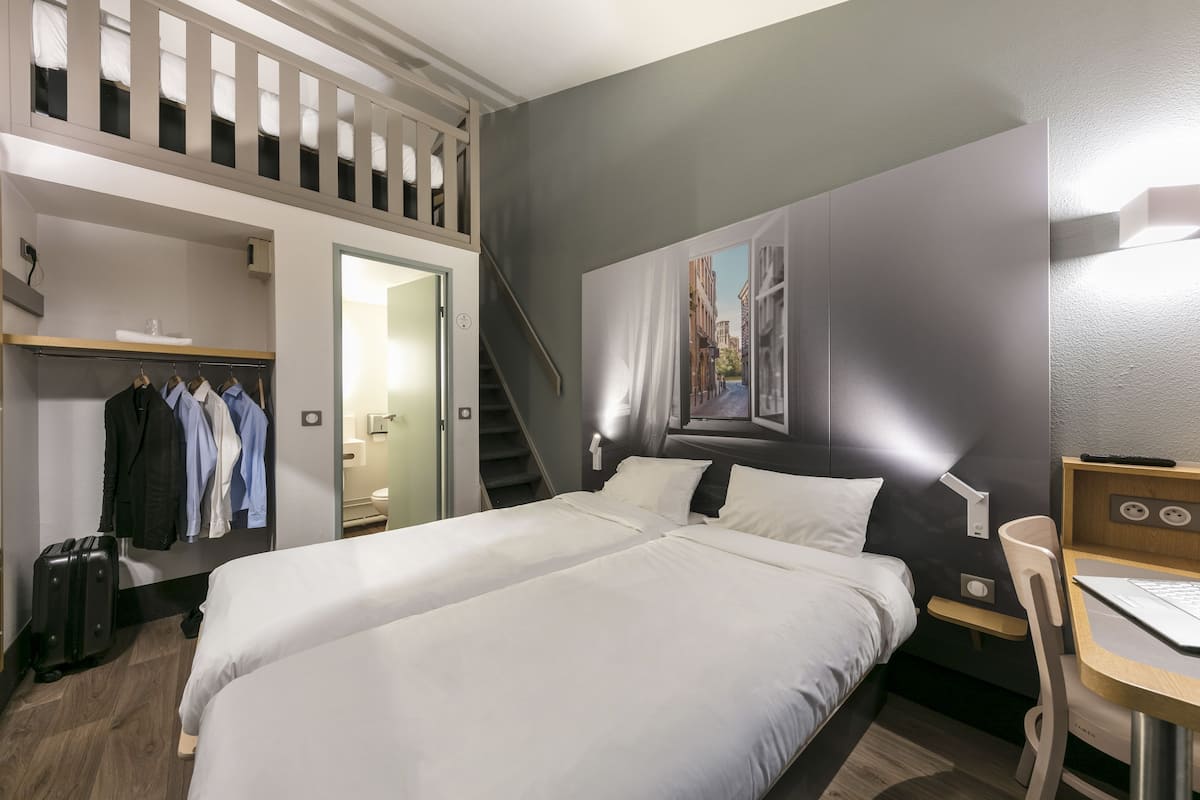 A hotel room with a large bed, a desk, a chair, a wardrobe, and a staircase.